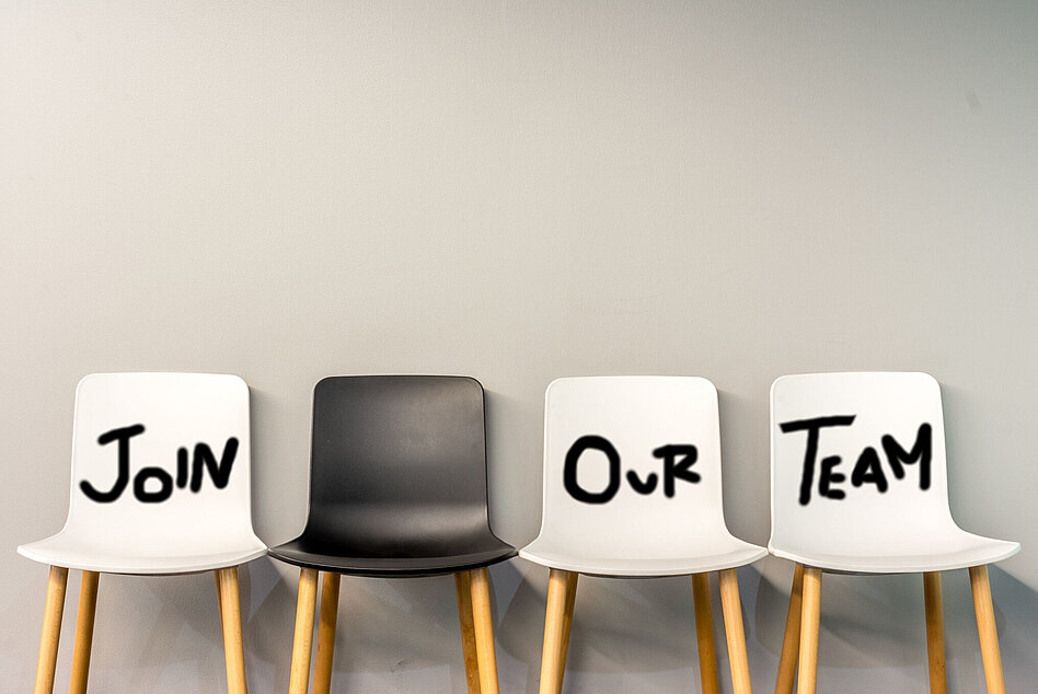 Four chairs (three white, one black) with "Join our team" written on the white ones