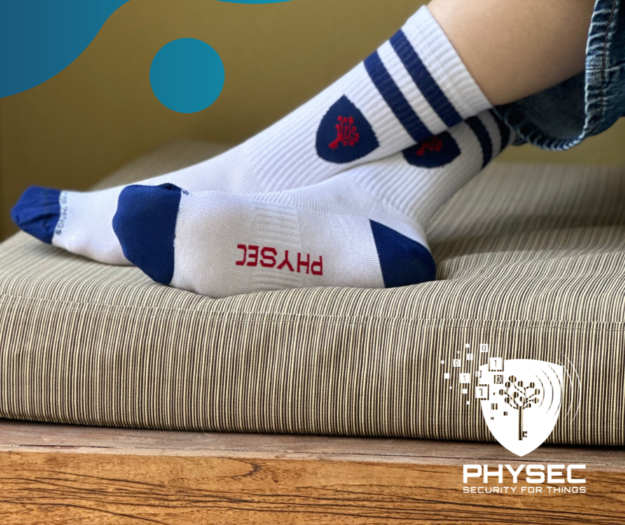 Das Bild zeigt die 2. Auflage der PHYSEC Socken. Die Tennissocken sind weiß mit blauem PHYSEC Logo und zwei blauen Streifen am oberen Ende