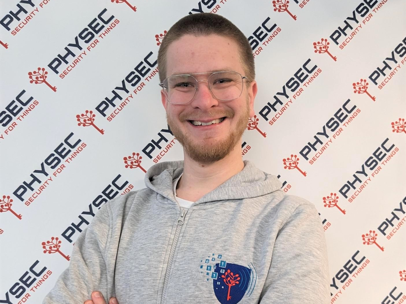 Porträt von Lars Peuckmann, der ein graues Kapuzensweatshirt mit dem Physec-Logo trägt