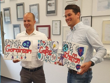 Geschäftsführer Heiko Koepke und Christian Zenger halten 3 Leinwände auf denen "Gemeinsam Großes Schaffen" steht
